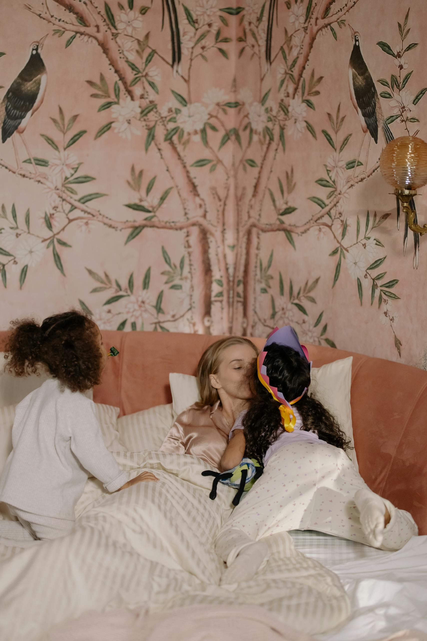 A loving morning moment as a mother bonds with her daughters in bed, surrounded by warmth.