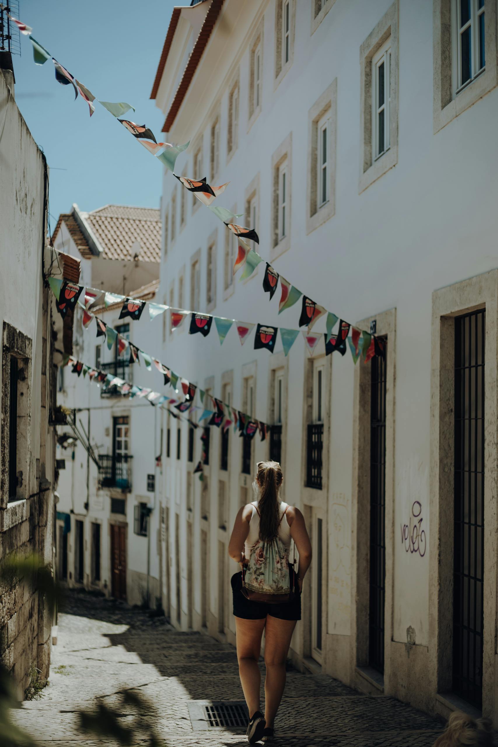 A woman walks down a narrow, decorated street in Lisbon, Portugal, capturing the city's historic charm.