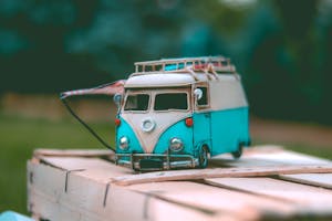Close-up of a vintage miniature blue van toy placed on a wooden surface outdoors, capturing a nostalgic scene.